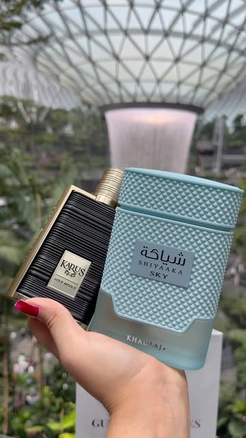 Khadlaj Karus and Shiyaaka Sky perfume bottles held in front of the Jewel waterfall
